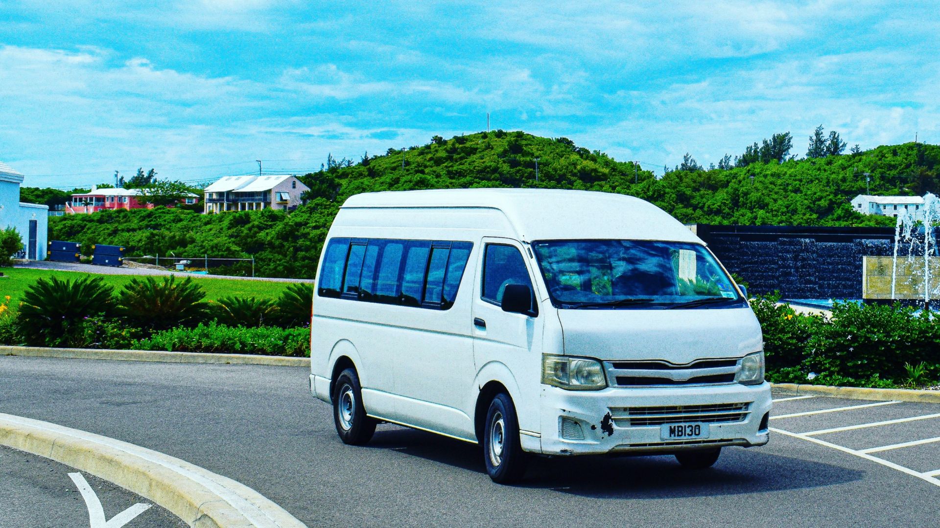 a white van driving down a street next to a lush green hillside