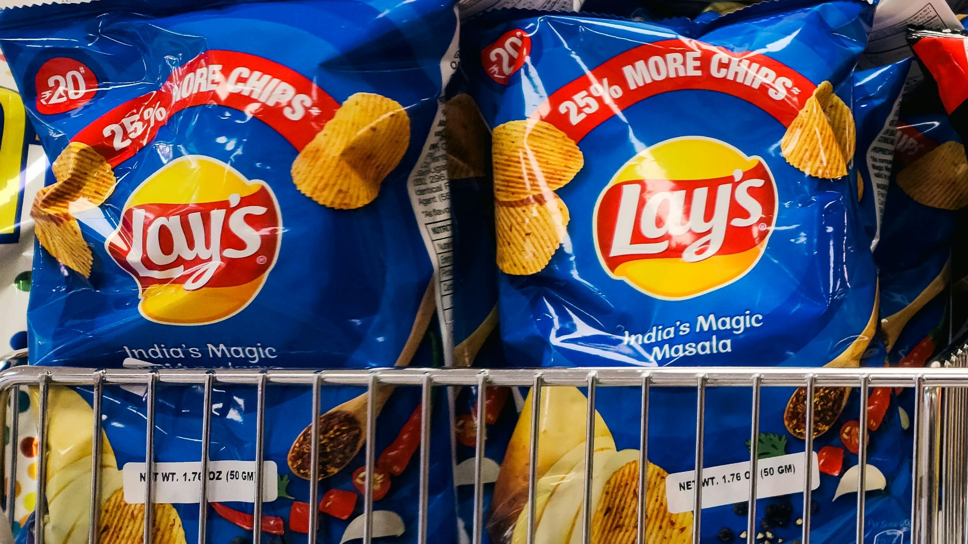 Bags of potato chips on a store shelf against a white tiled wall