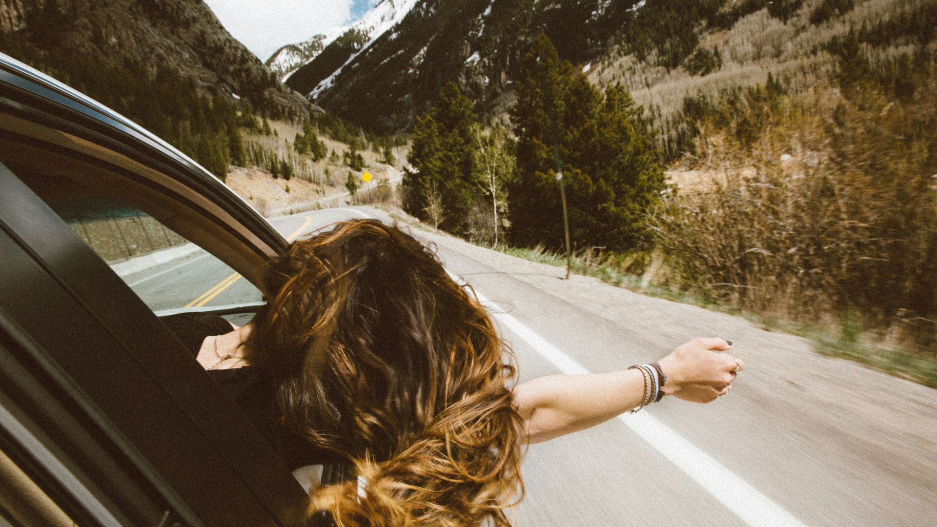 woman riding on vehicle putting her head and right arm outside the window while travelling the road