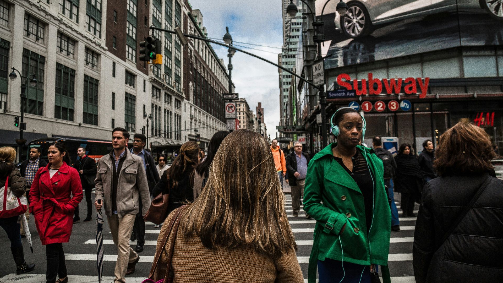 woman wearing green jacket walking on the pedestrian lane during daytime