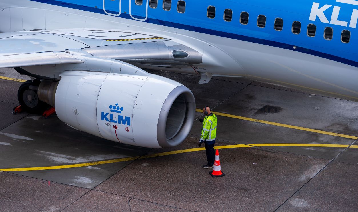 A KLM aircraft undergoing maintenance on the tarmac with an engineer inspecting it.