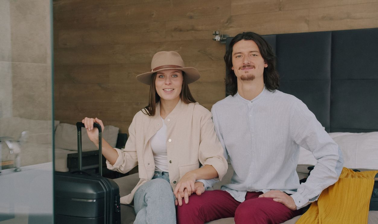 A young couple sitting in a stylish hotel room with luggage, ready to explore the city.