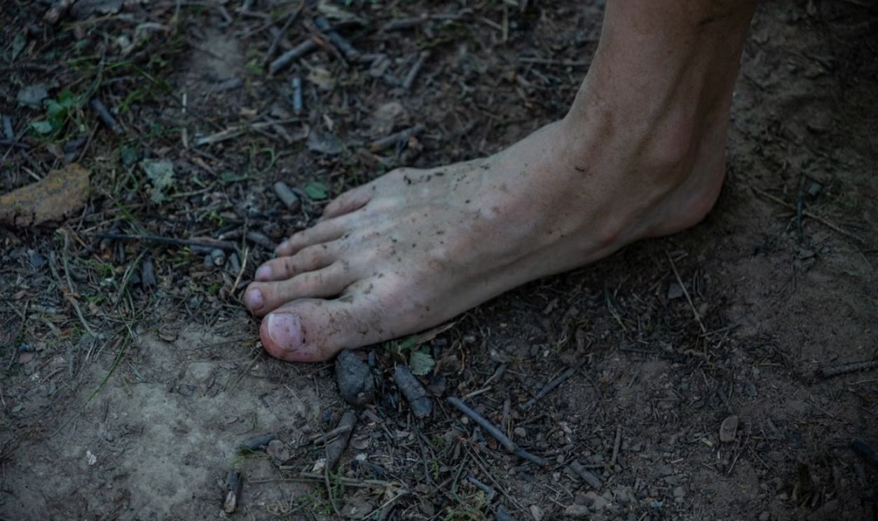 A bare foot on muddy ground among twigs and leaves outdoors