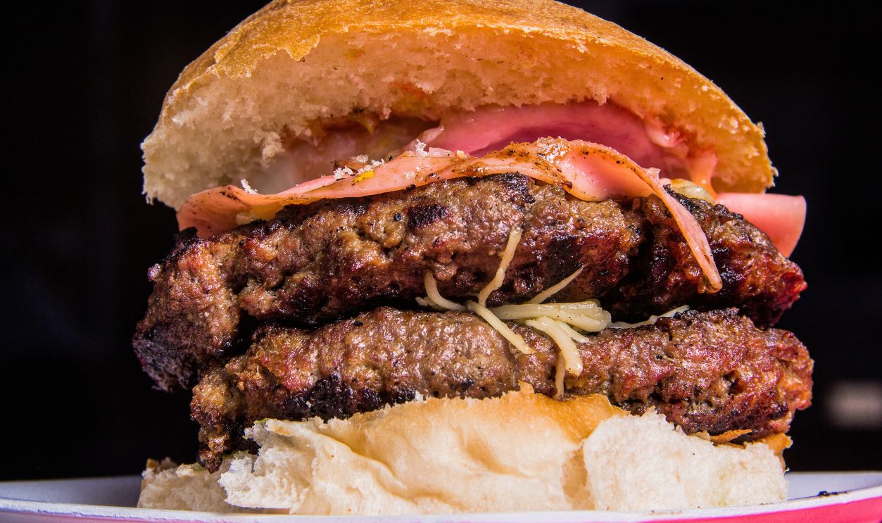 A towering, mouth-watering burger featuring multiple beef patties, layers of ham, and fresh toppings, all nestled between a soft, golden bun, perfect for any meat lover.