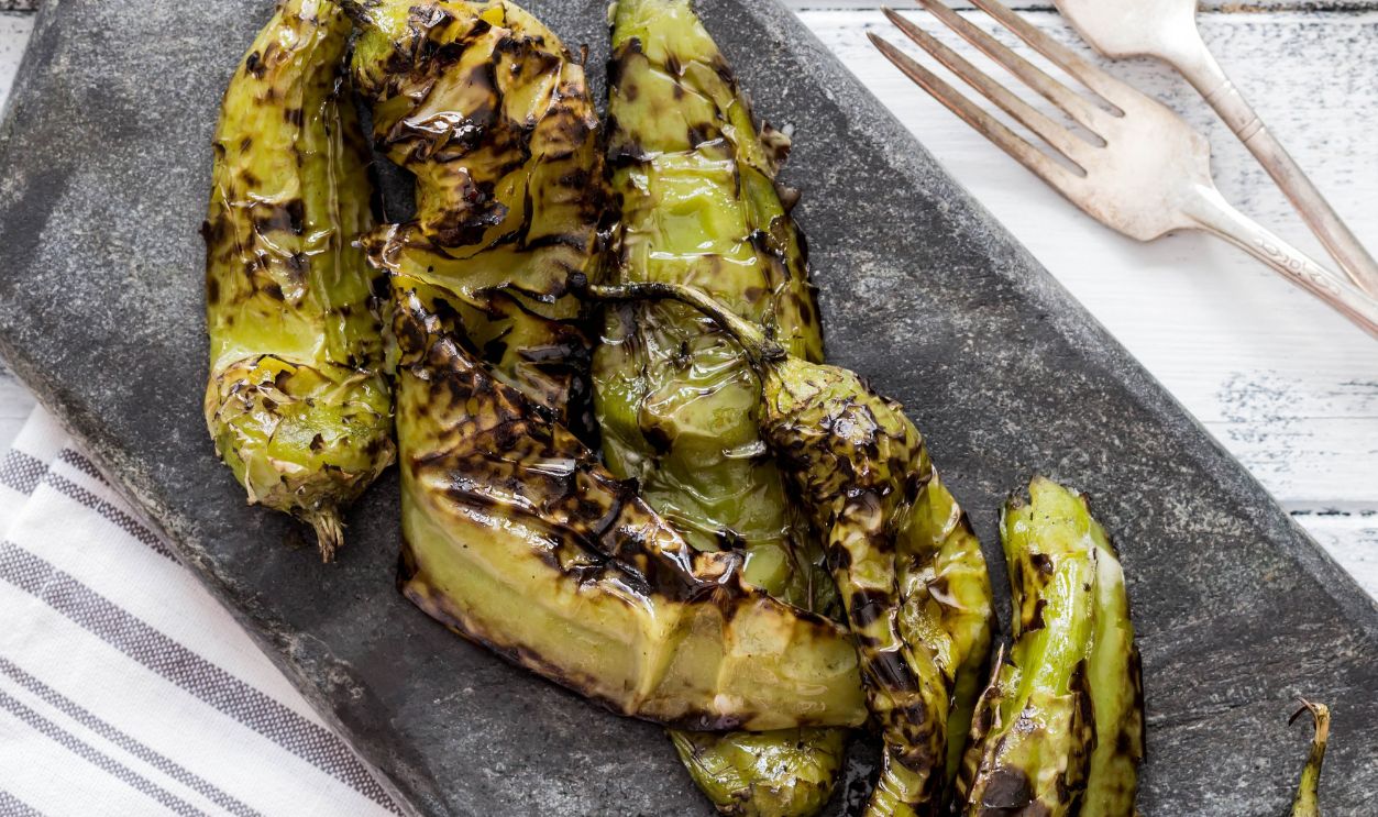 Roasted hatch chili peppers on the cutting board. Fall harvest. Summer menu. Rustic style. Vegetarian menu. Green chilies. Hatch Chile Festival.