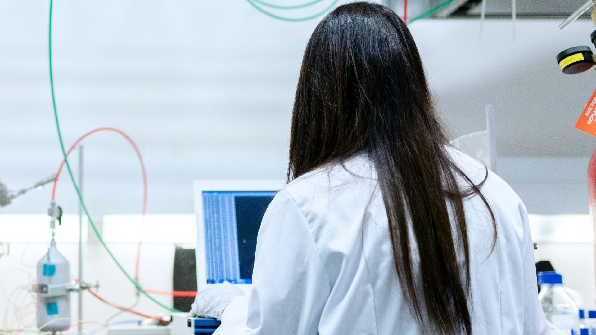 A scientist in a white lab coat using a laptop in a laboratory