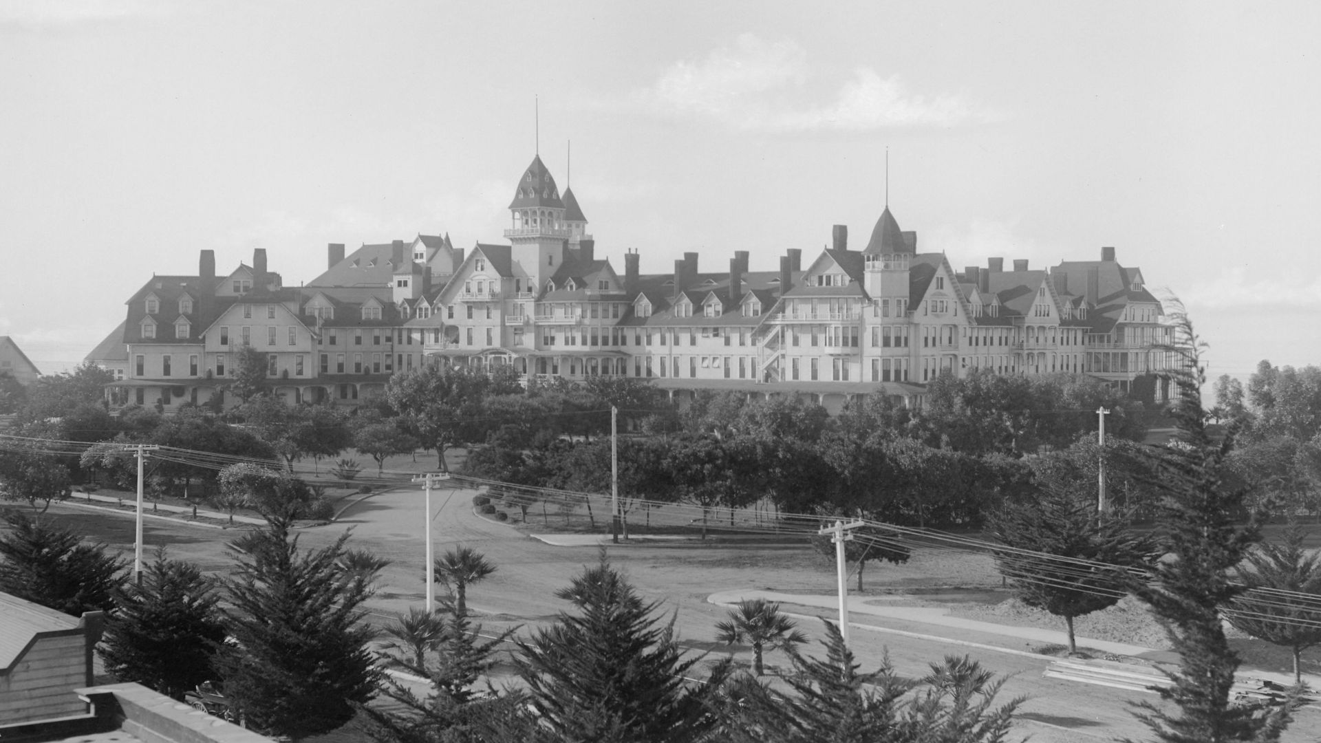 Hotel Del Coronado, ca.1898-1900
Photograph of Hotel Del Coronado, San Diego, ca.1898-1900. A broad avenue lined with trees and utility poles and lines runs in front of the hotel. The grounds on which the large building stands has many trees. The Pacific 