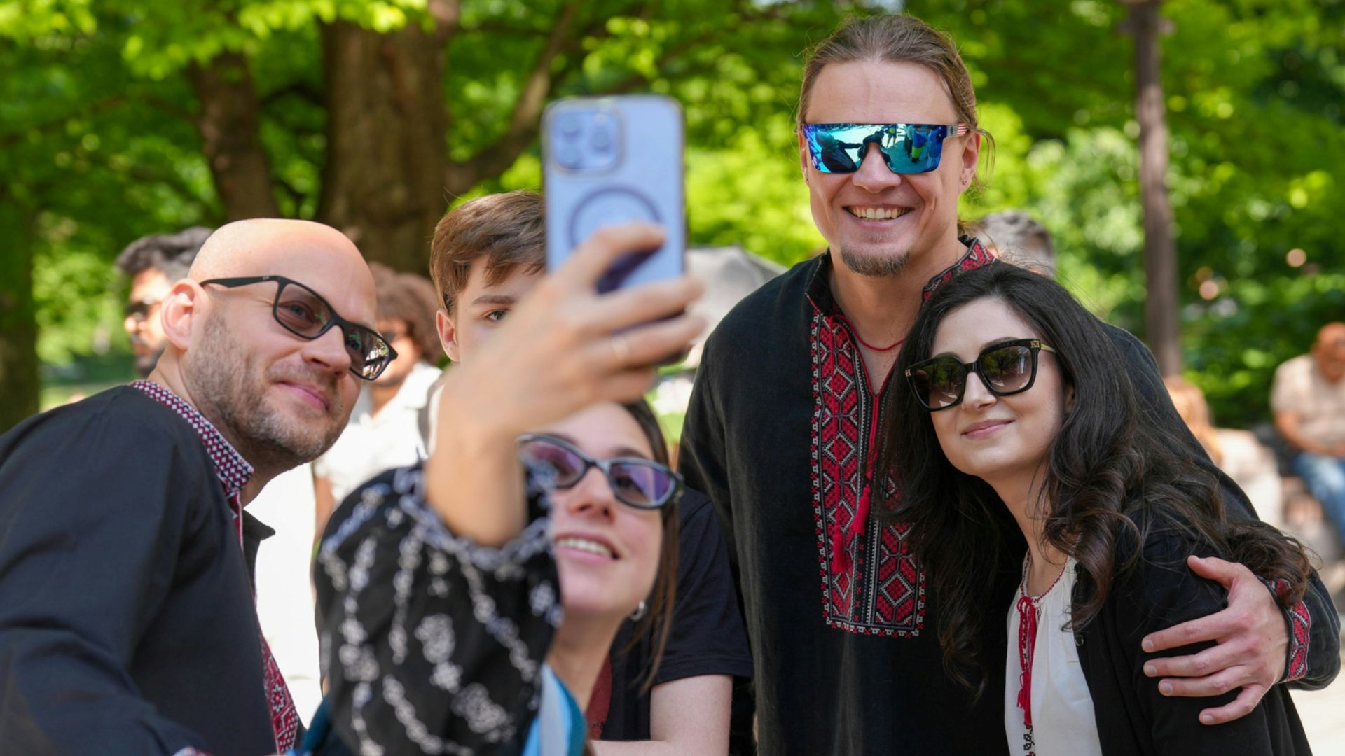 A group of people in embroidered shirts taking a selfie in a park