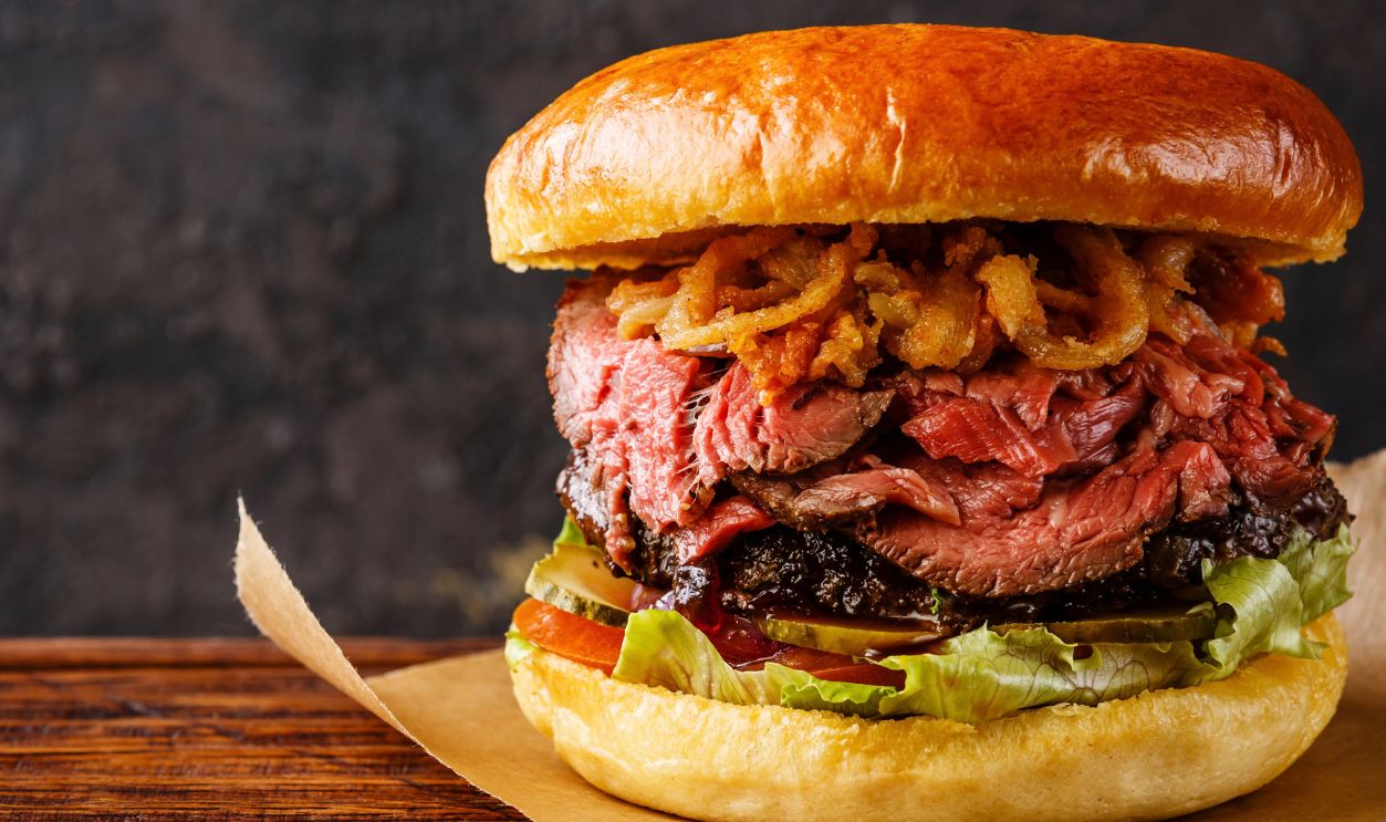 Pastrami Burger with sliced Roast beef and onion fries rings on black background