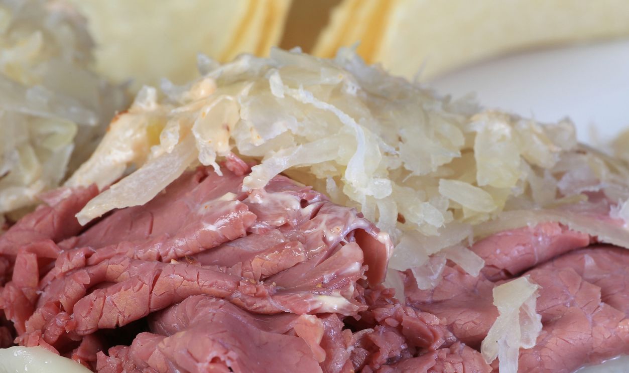 Corned Beef piled high on pumpernickel bread with sauerkraut and swiss cheese to create Reuben Sandwich.