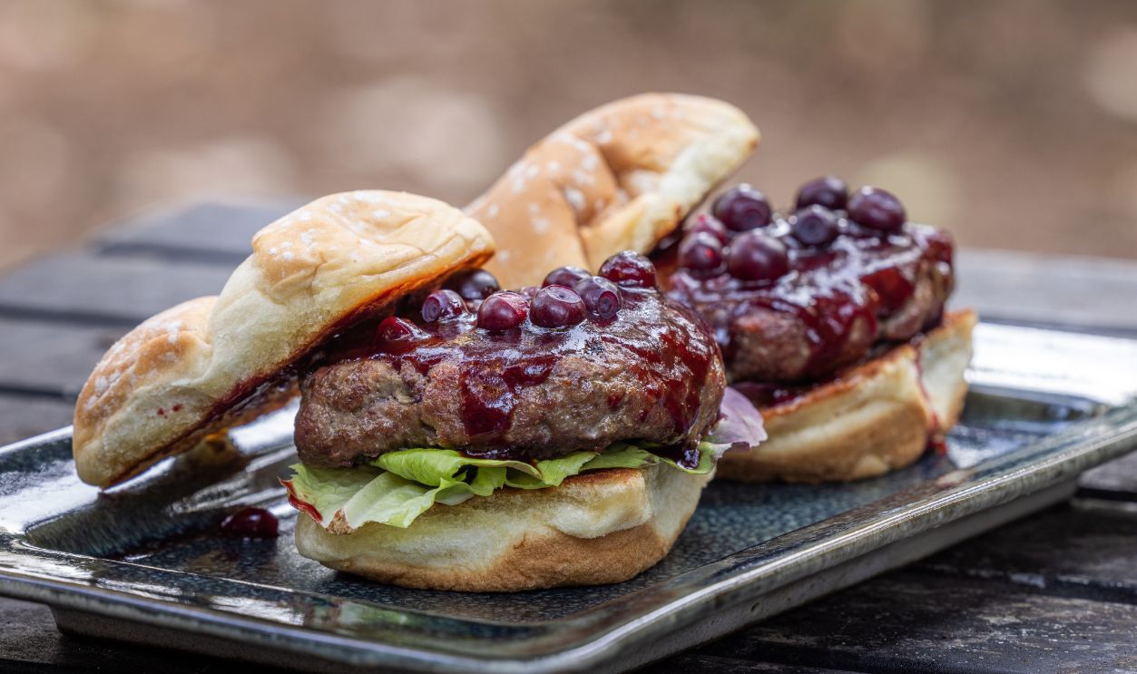 Fresh grilled beef burgers topped with a huckleberry bbq sauce and fresh huckleberries served outdoors