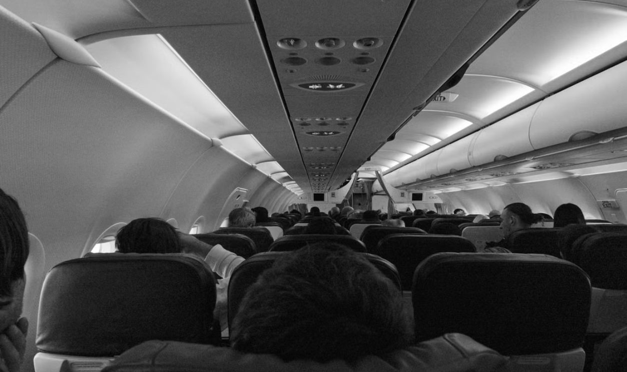 Black and white view of passengers seated inside an airplane cabin