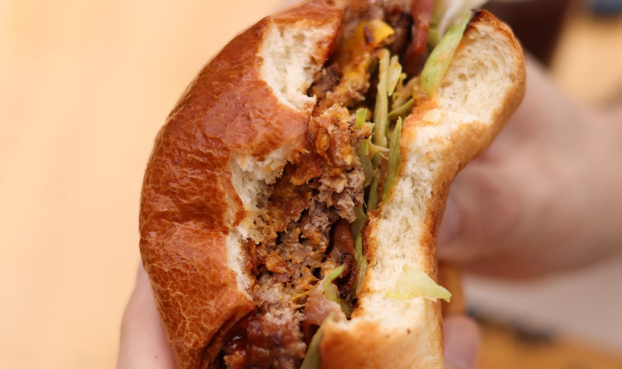 Close-up of a person holding a juicy cheeseburger with visible layers and ingredients