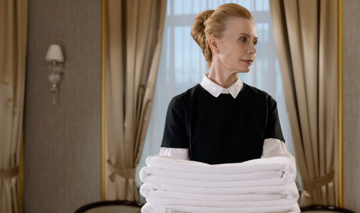 Elegant hotel housekeeper holding fresh, neatly folded white towels in a luxurious room.