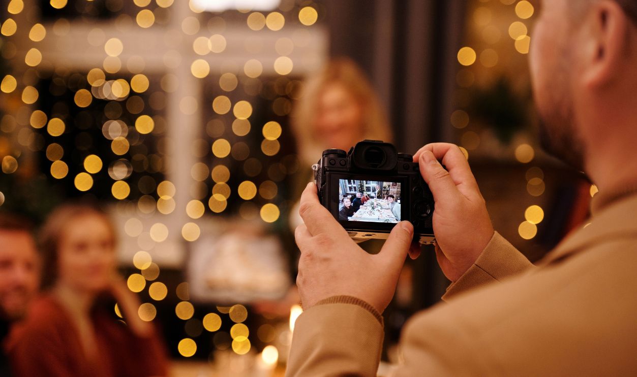 Man capturing a family dinner gathering with a camera surrounded by warm festive lights.
