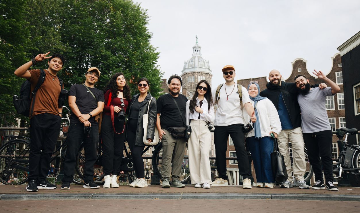 Diverse group of tourists posing in Amsterdam with a historic building backdrop.