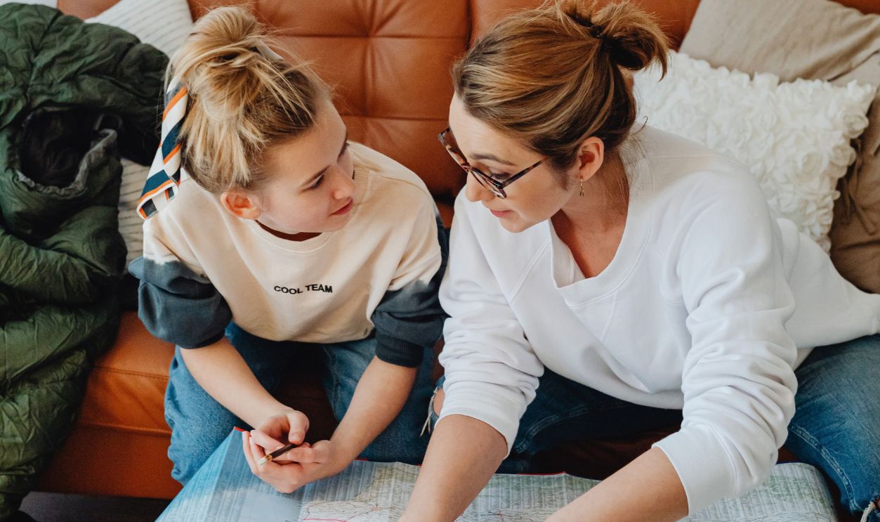 A mother and daughter sitting on a sofa planning travel with a map, sharing a meaningful conversation.
