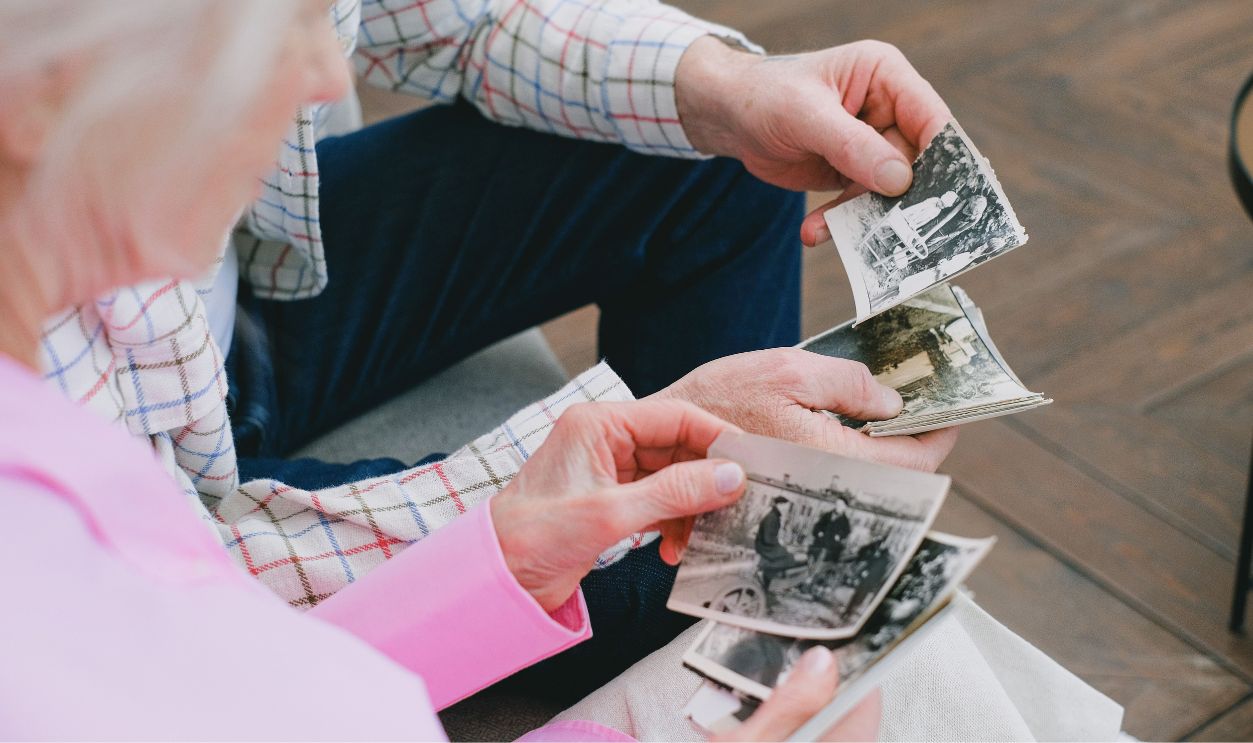 Elderly couple reminiscing over vintage black and white photographs, exploring memories.
