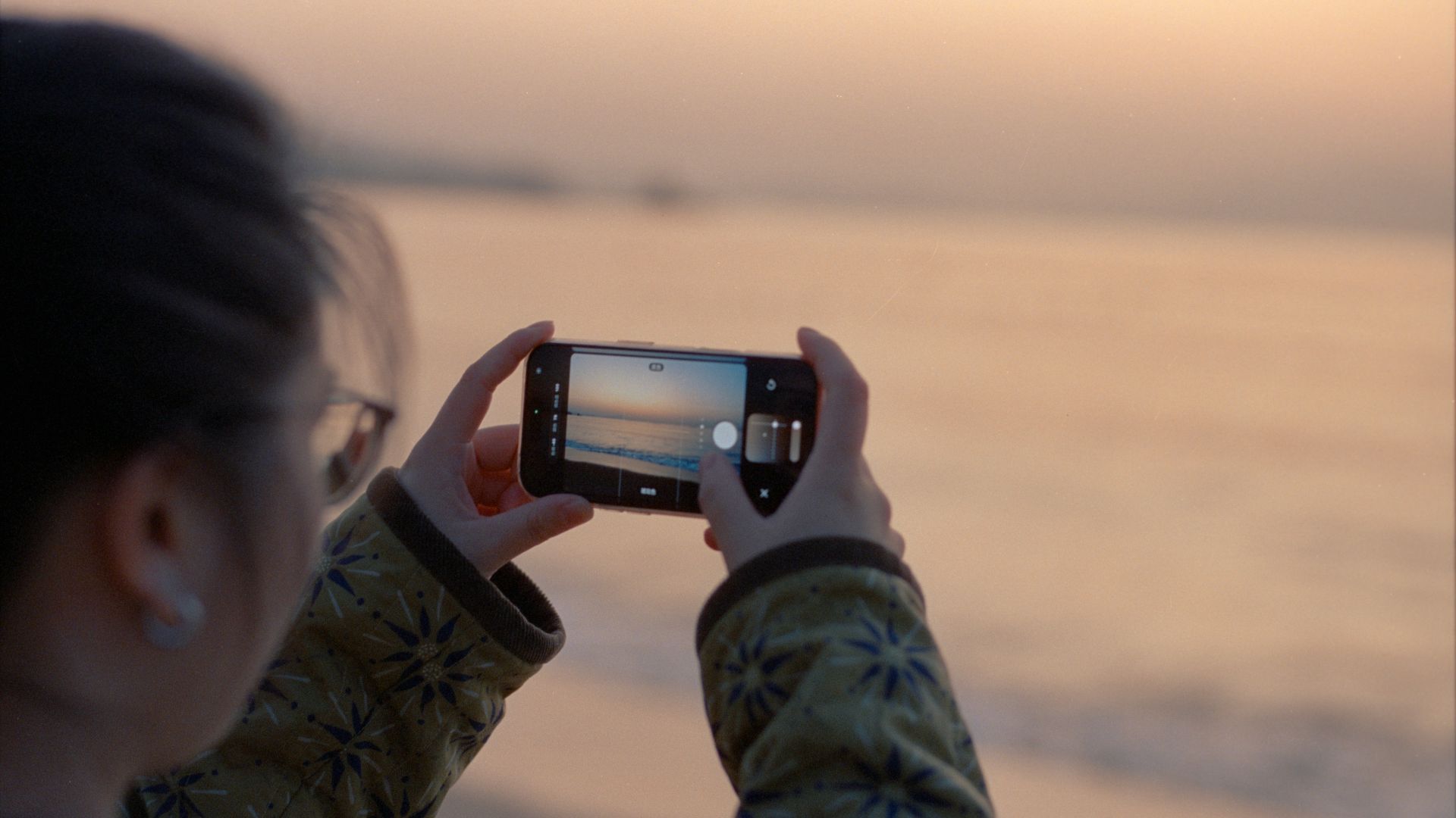 Woman taking a picture of the ocean at sunset
