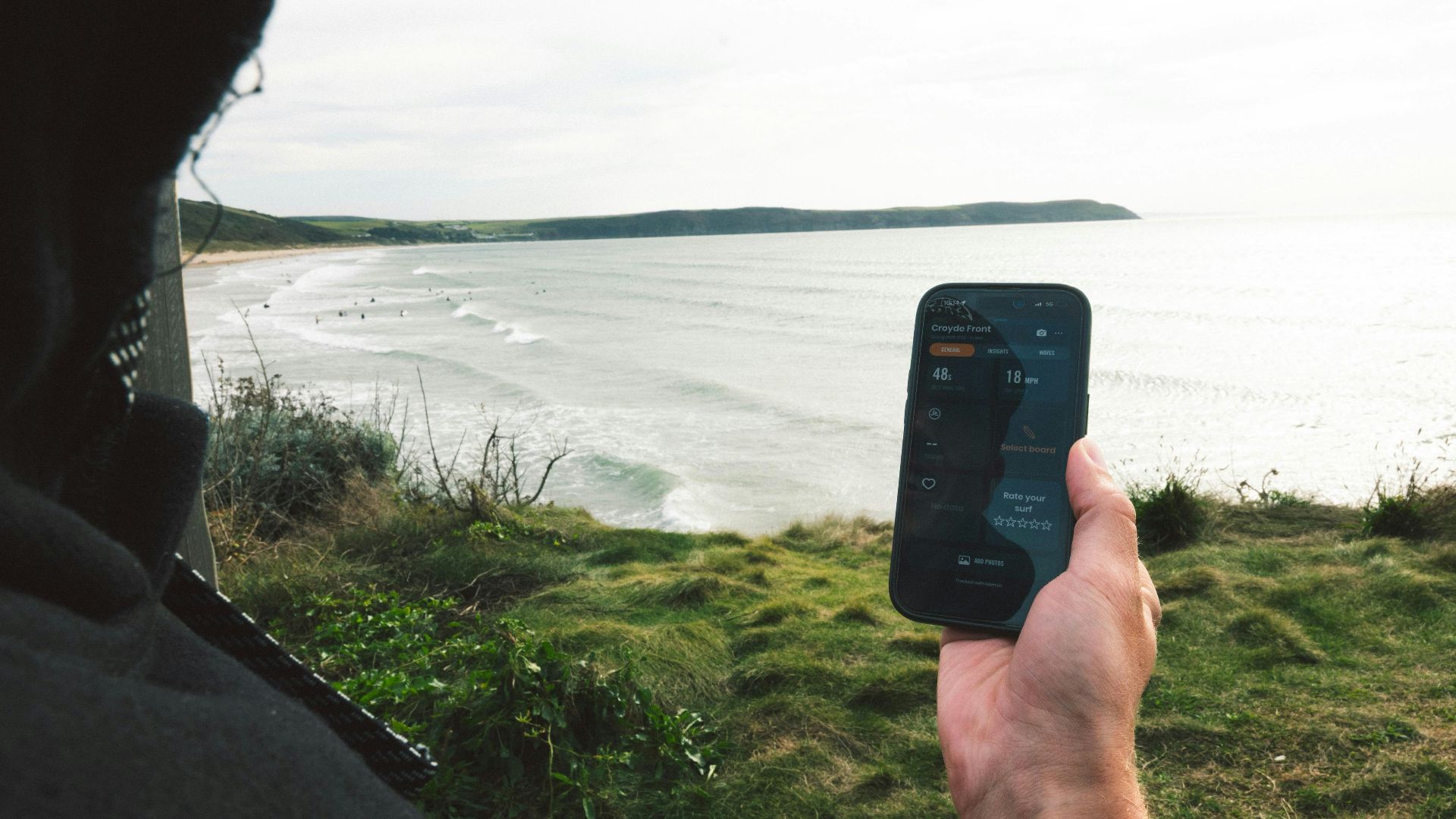 Person holding phone overlooking ocean and beach