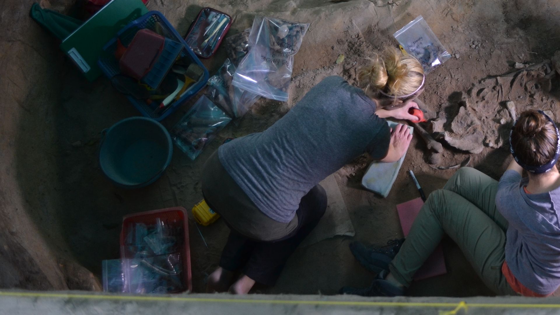 Overhead photo of an excavation trench showing four archaeologists working to excavate a burial from the Prei Khmeng site.