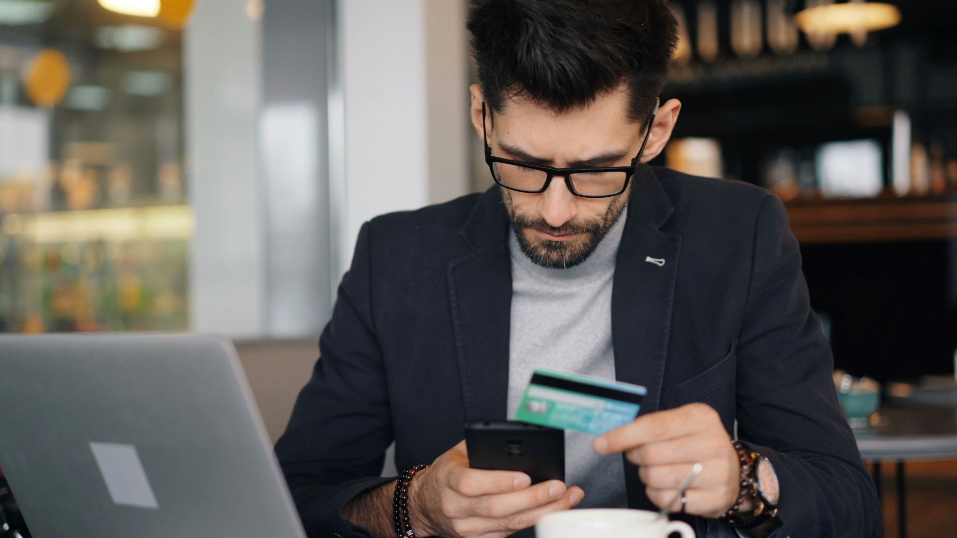 a man sitting at a table looking at his cell phone and holding a credit card