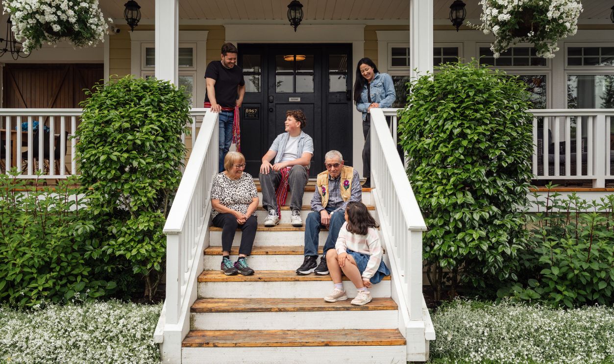 Multigenerational family enjoying a moment on porch steps surrounded by greenery.