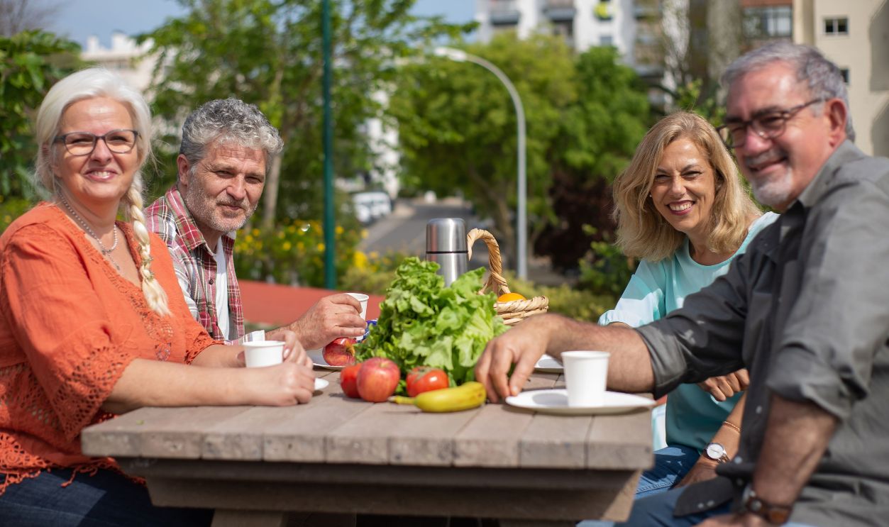 A group of seniors enjoying a sunny outdoor picnic in Portugal, socializing and smiling.