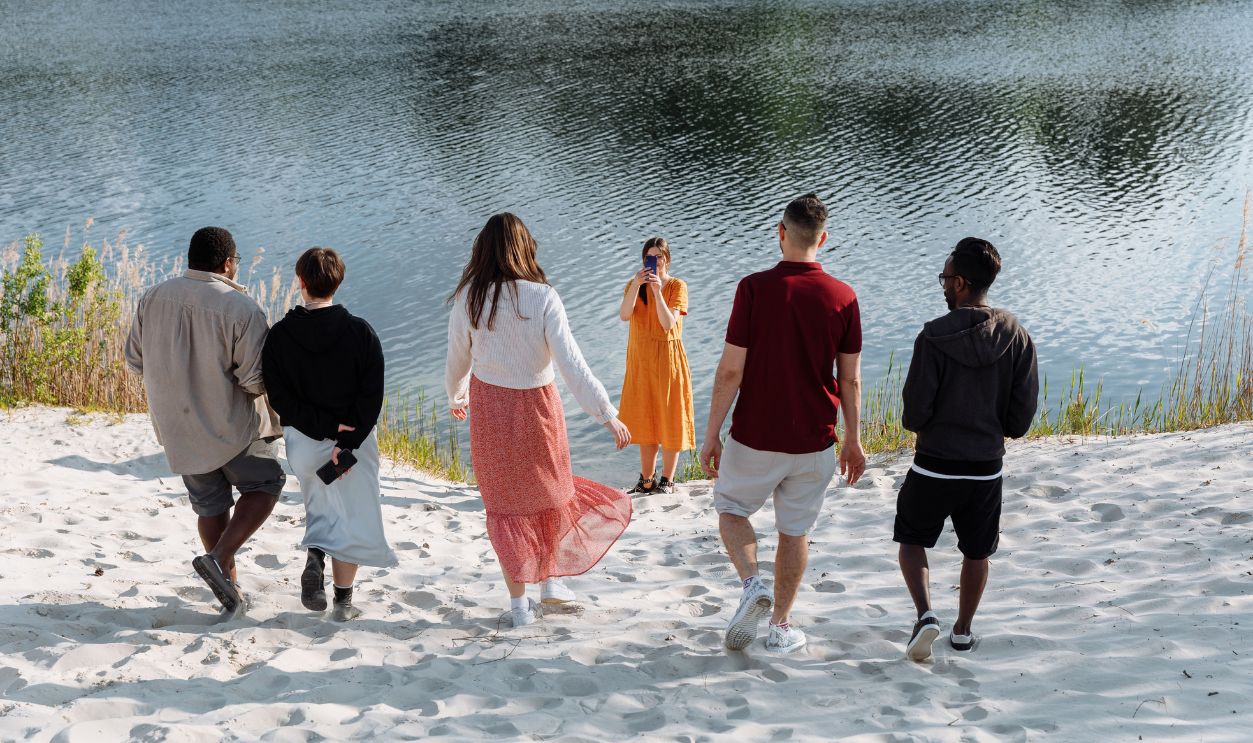 A group of friends enjoy a sunny day near a calm lake, capturing memories on a sandy beach.