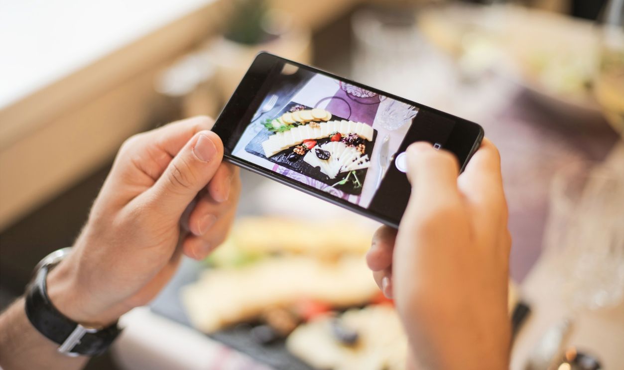 Hands holding a smartphone capturing a photo of a plated dish in a cozy setting.