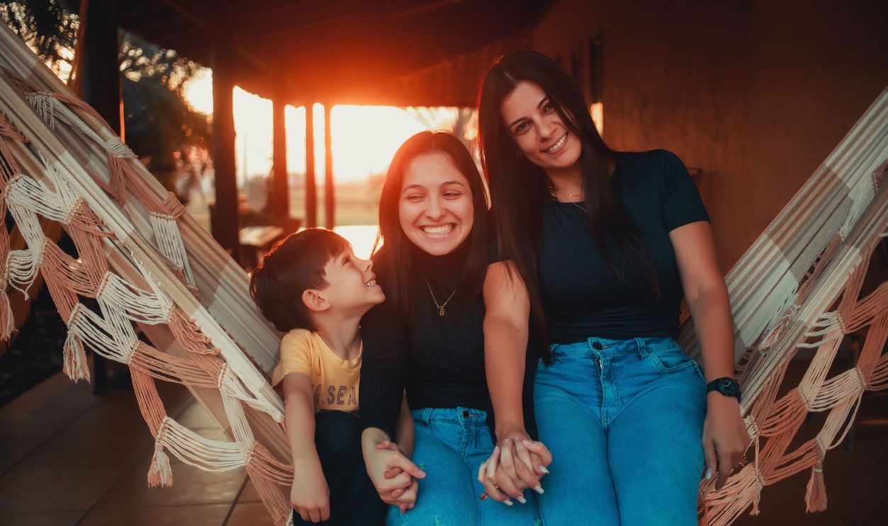 A joyful family moment with three smiling individuals on a hammock during sunset.
