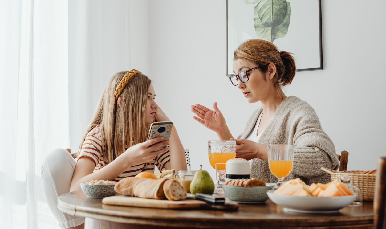 Mother and daughter enjoying breakfast with fresh juice and pastries at home.