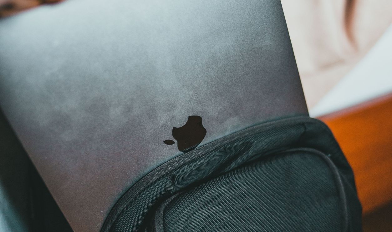A close-up of a person placing a laptop into a black backpack indoors.