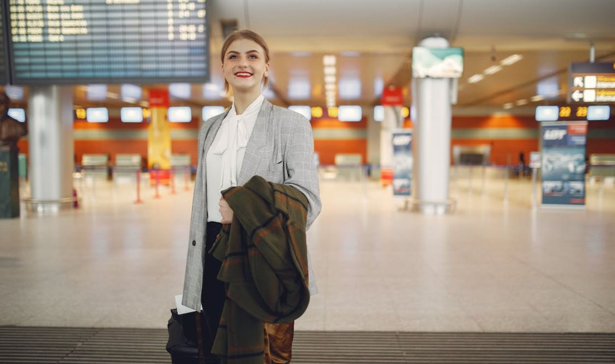 Happy young woman standing with baggage near departure board in airport