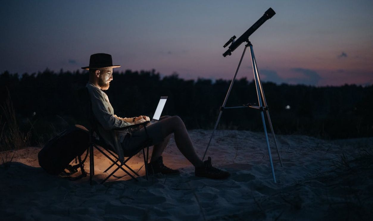 Man Camping in Wilderness with Laptop and Telescope
