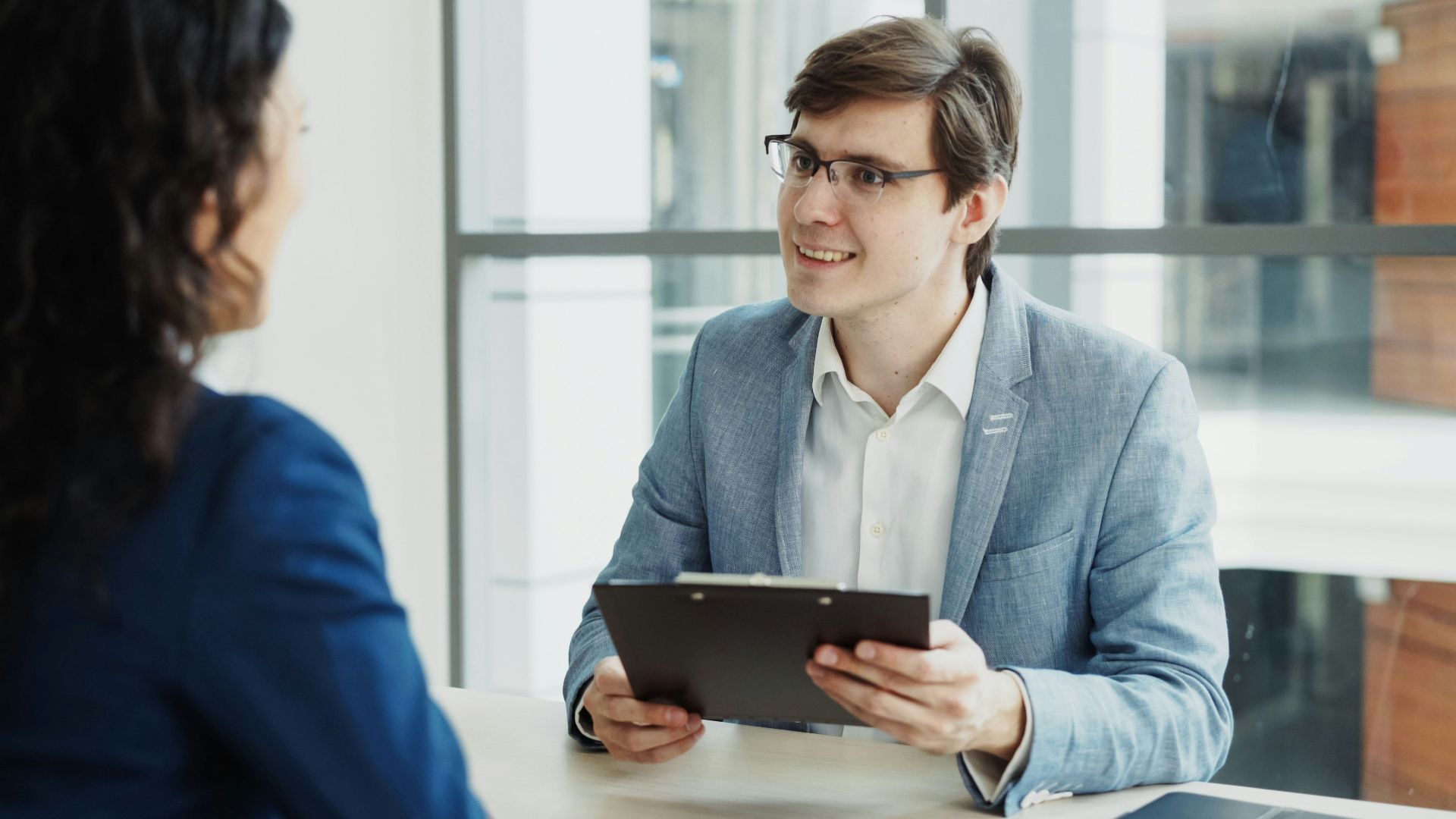 Man in suit interviews woman holding clipboard.