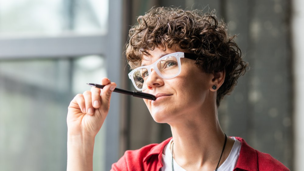 Young pensive female in eyeglasses thinking of new creative ideas
