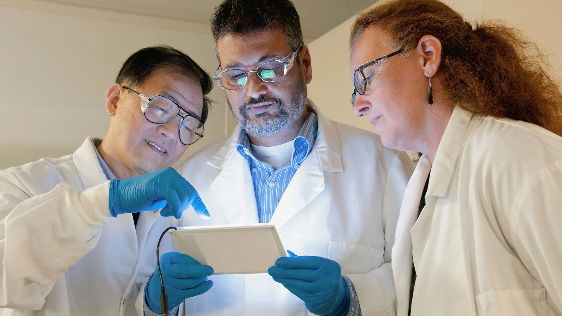 three people in lab coats looking at a tablet