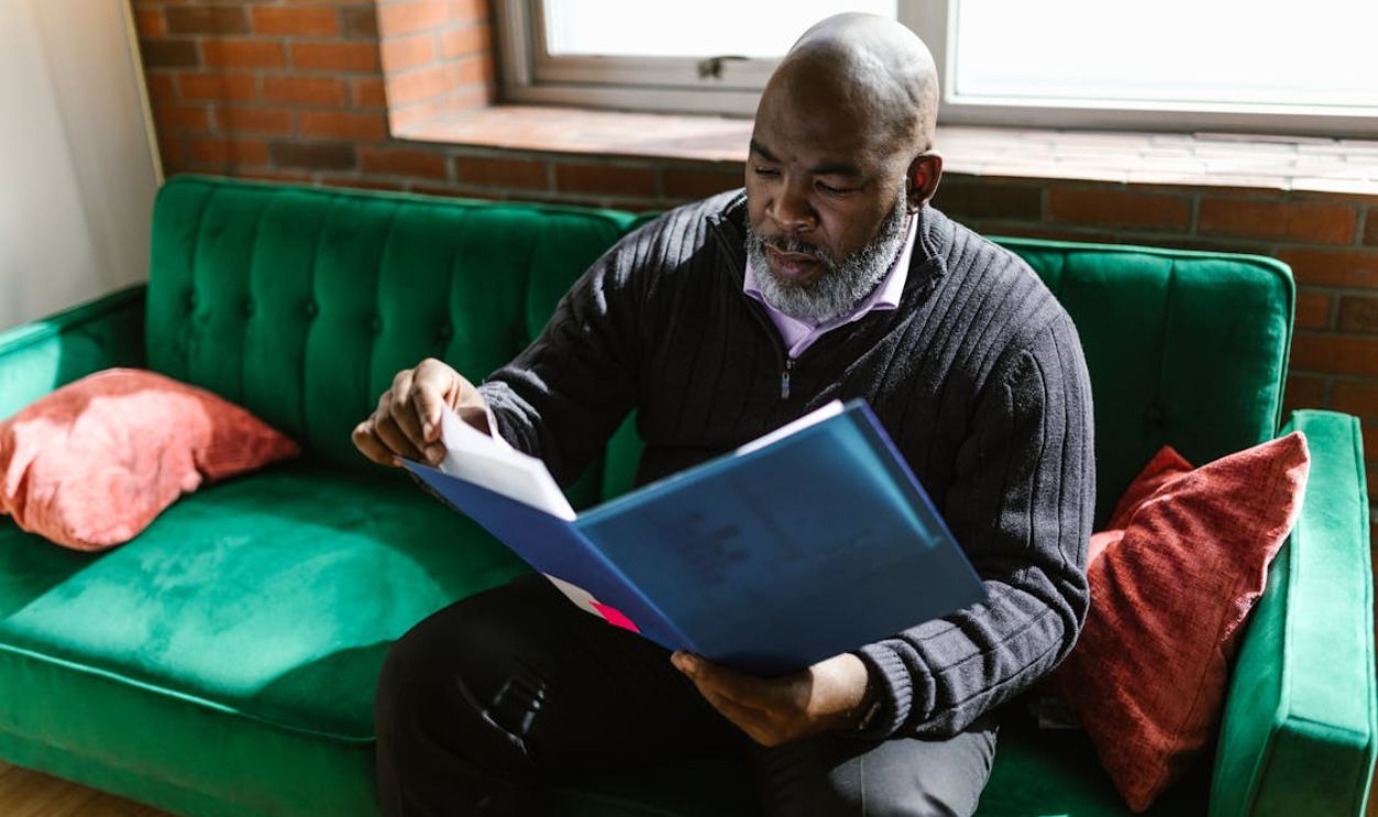 A Man Sitting on Green Couch while Looking Documents