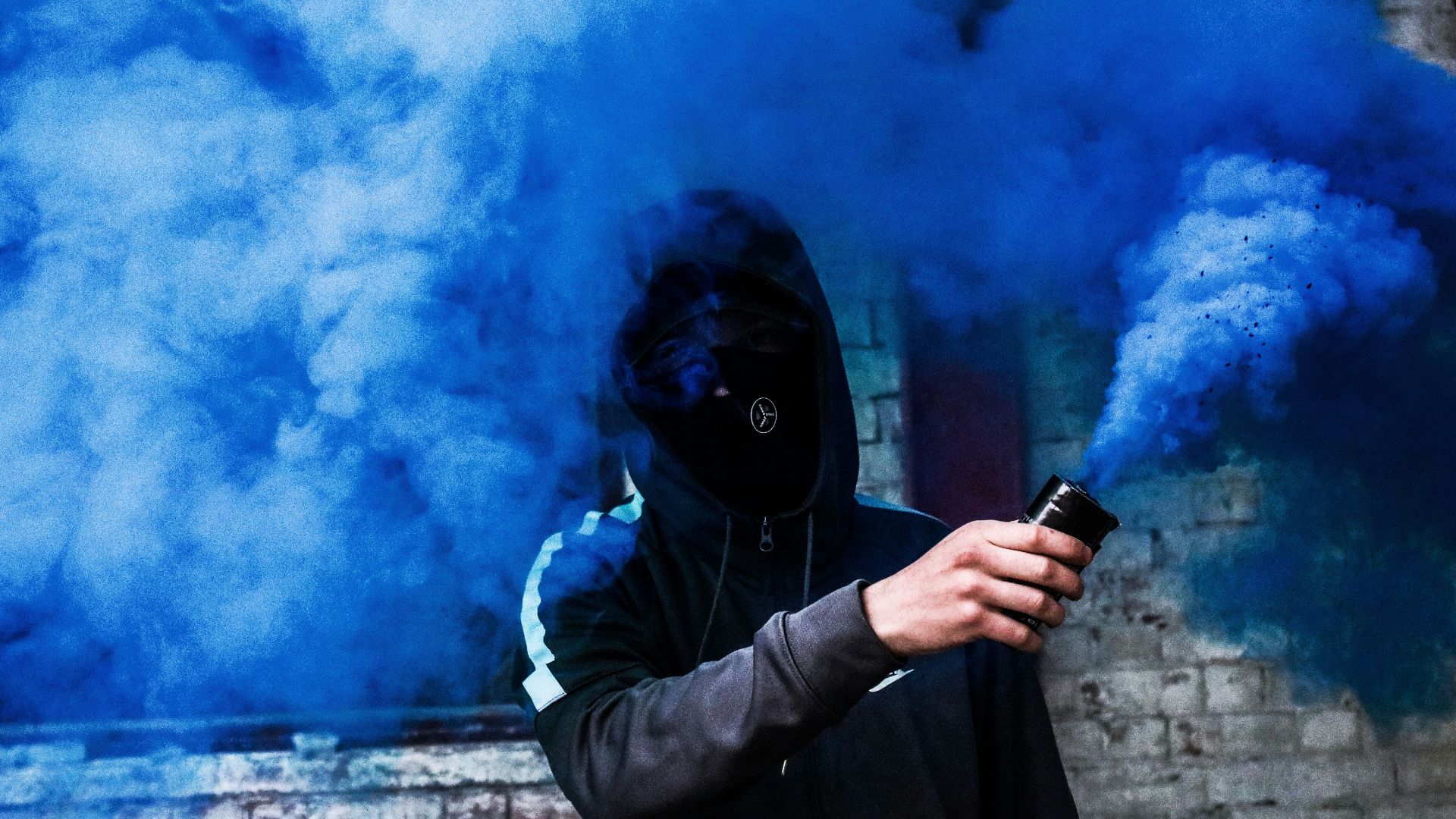 person covered with mask and hoodie using blue smoke