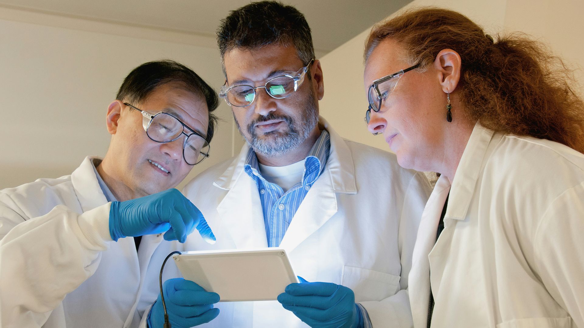three people in lab coats looking at a tablet