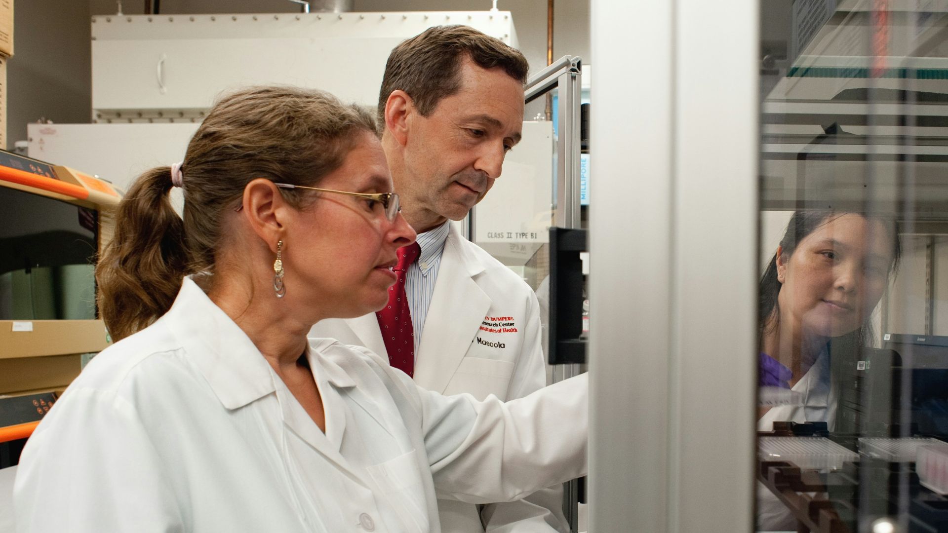 a man and a woman in lab coats looking at something in a cabinet