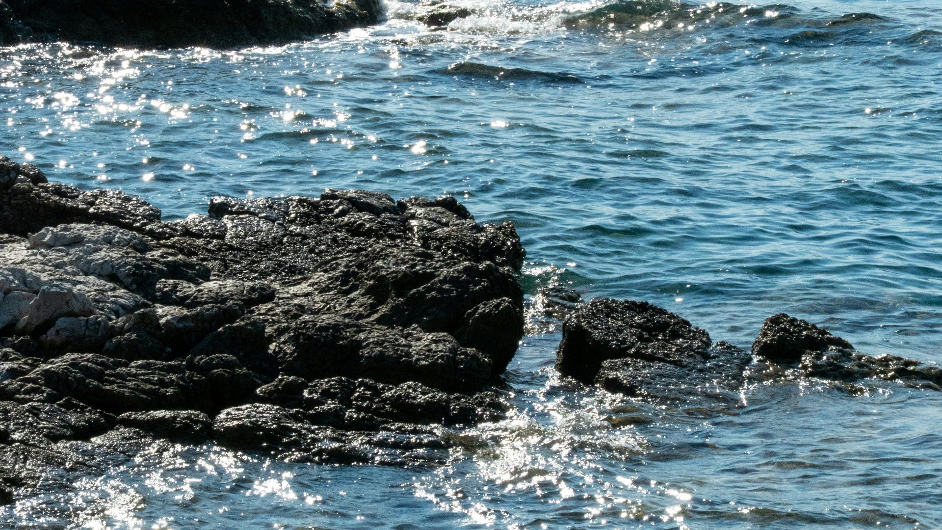 Sparkling blue ocean water laps against rocky shore