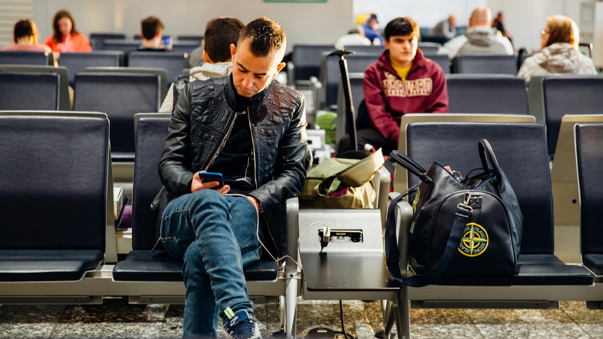 People sitting in an airport lounge, focused on smartphones and waiting for flights.