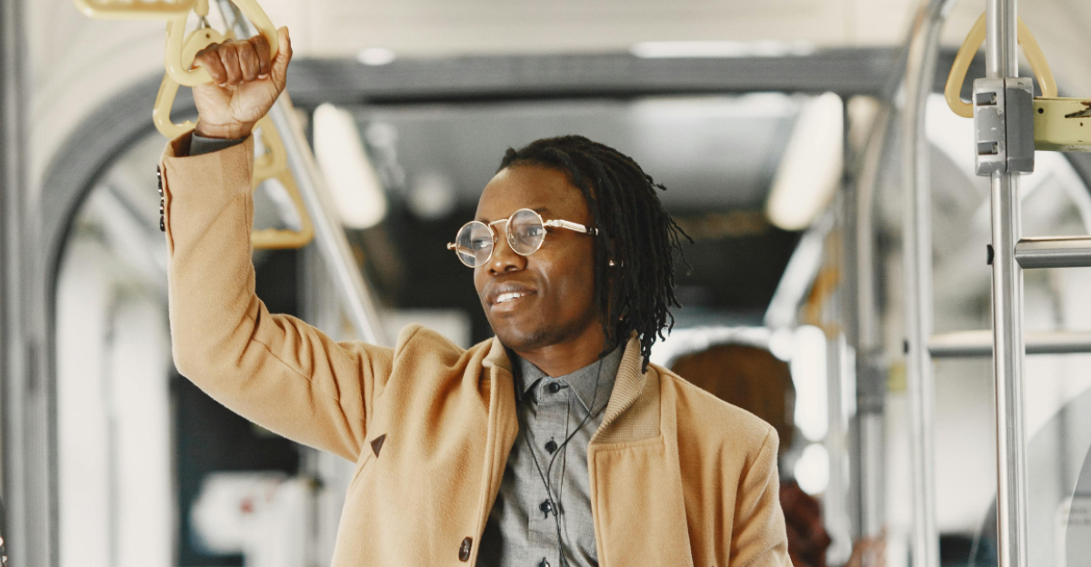 man-in-brown-coat-holding-on-bus-handle-while-holding-a-book