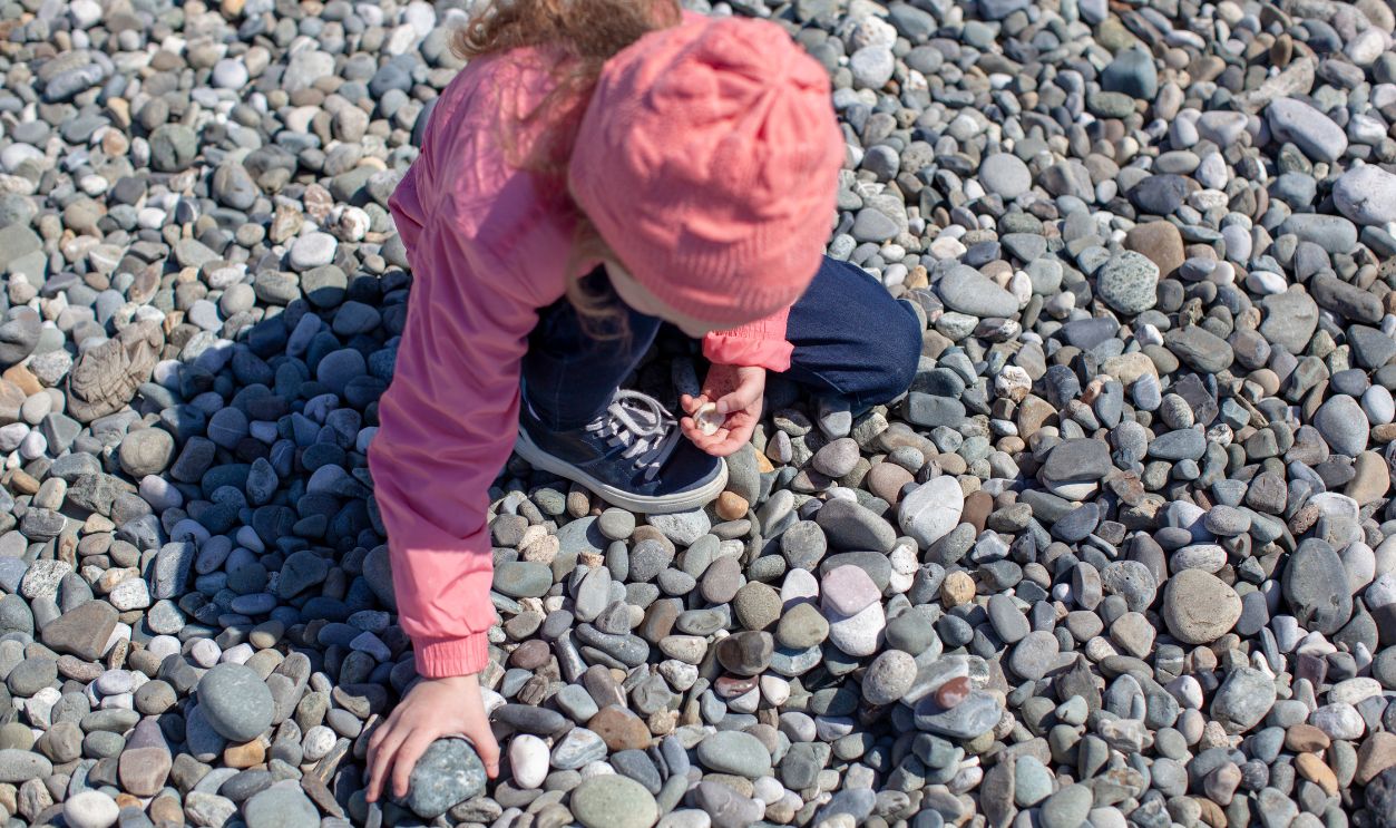 Five-year-old girl playing on the beach with rocks, the sea shore in spring