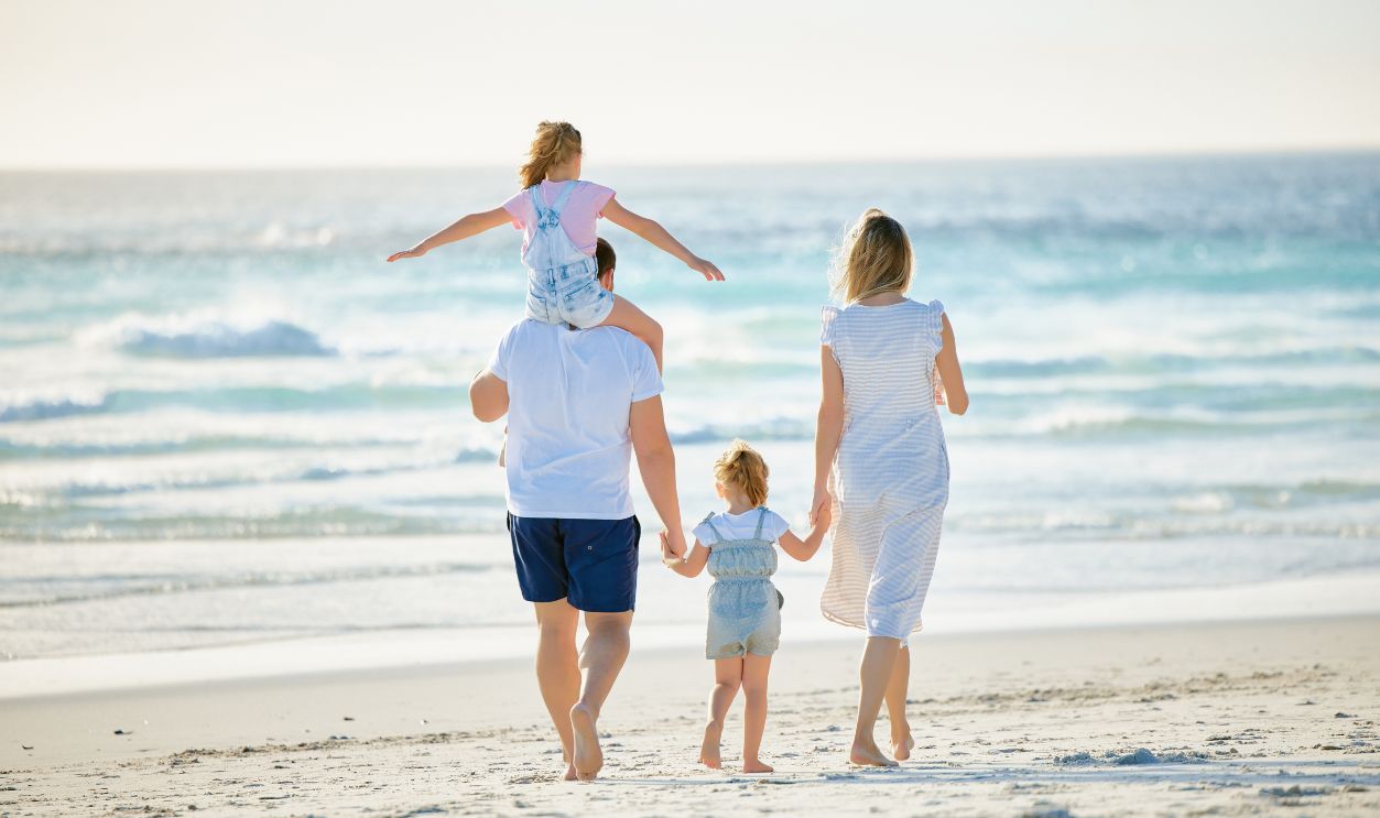 Happy family walking the beach. Rear view of young parents with children having fun on vacation. Little boy and girl enjoying summer with mother and father