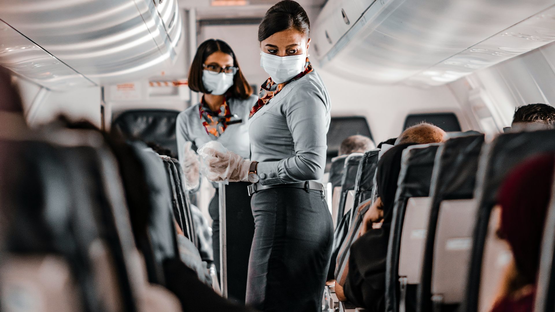 air hostess wearing a facemask standing in the aisle of an aeroplane