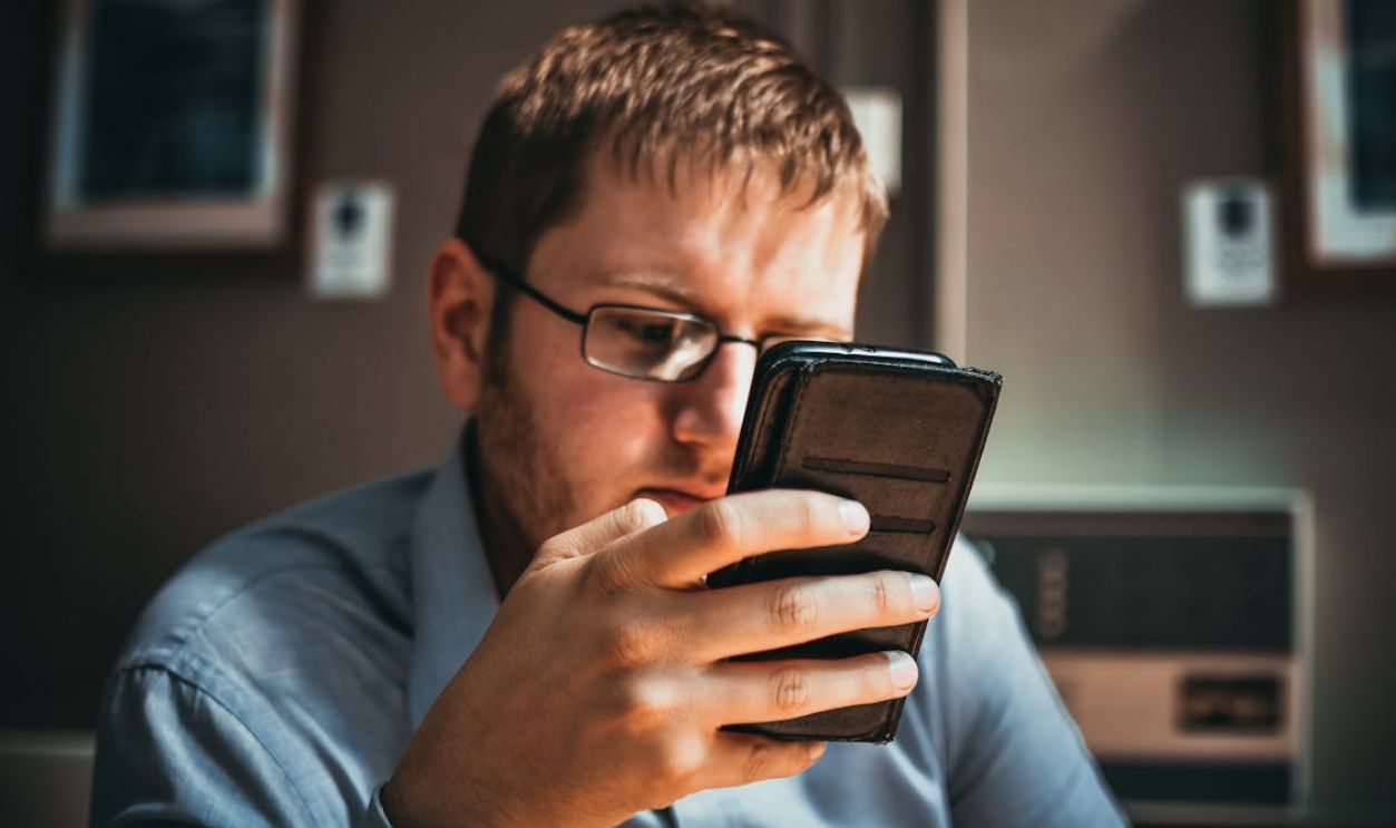 Man Using Phone Near Brown Wall