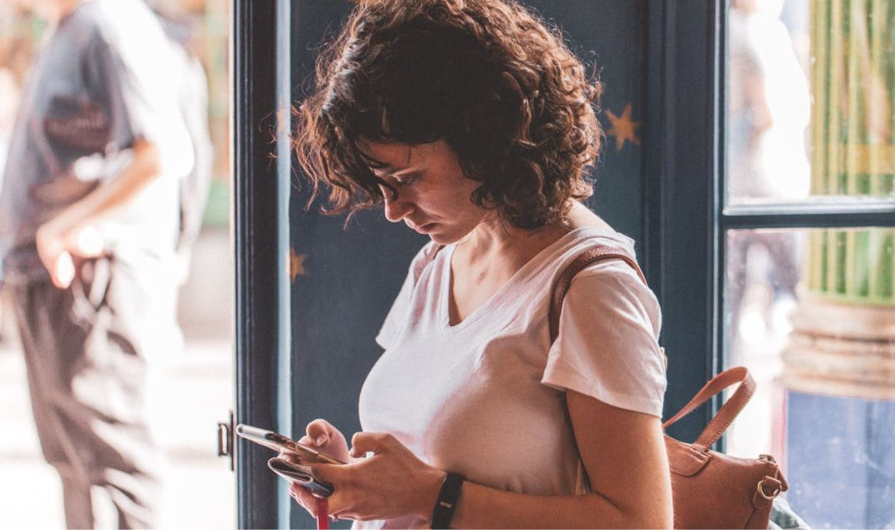 Curly Haired Woman in White T-Shirt Using her Smartphone